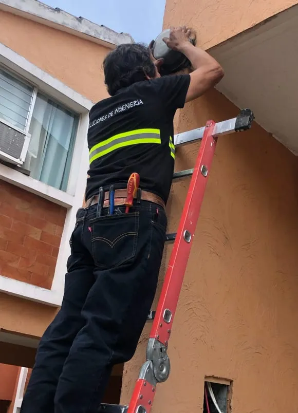 Técnico de SDI con chaleco reflectivo trabajando sobre una escalera junto a la fachada de un edificio