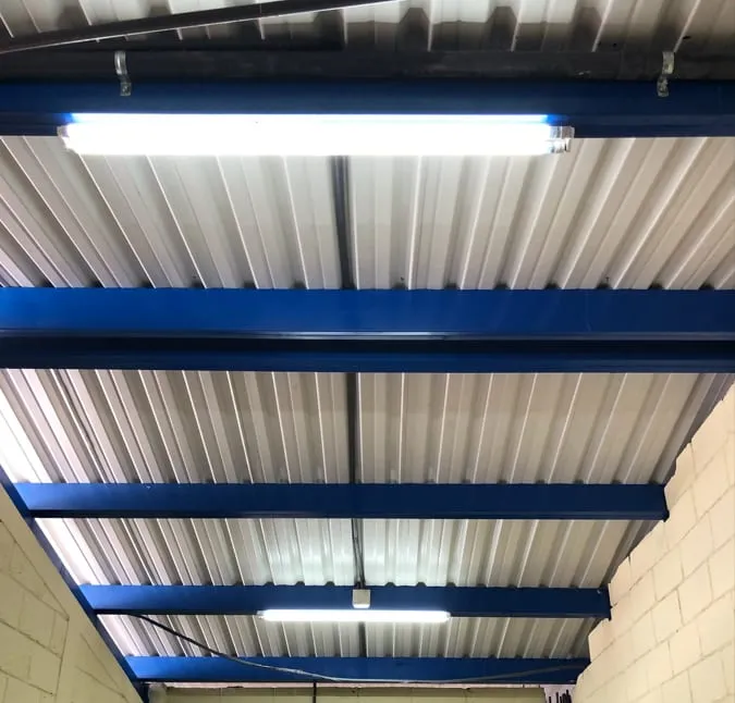 Luminaria LED lineal instalada bajo una cubierta metálica con estructura azul