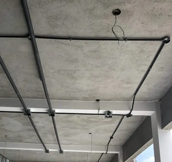 Tuberías eléctricas metálicas sobre el techo de concreto de un corredor