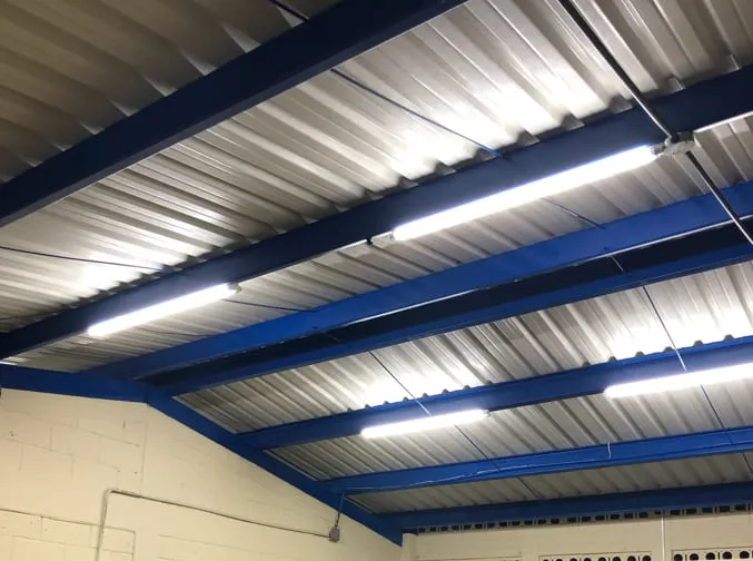 Luminarias LED lineales bajo el techo metálico de una edificación con estructura azul