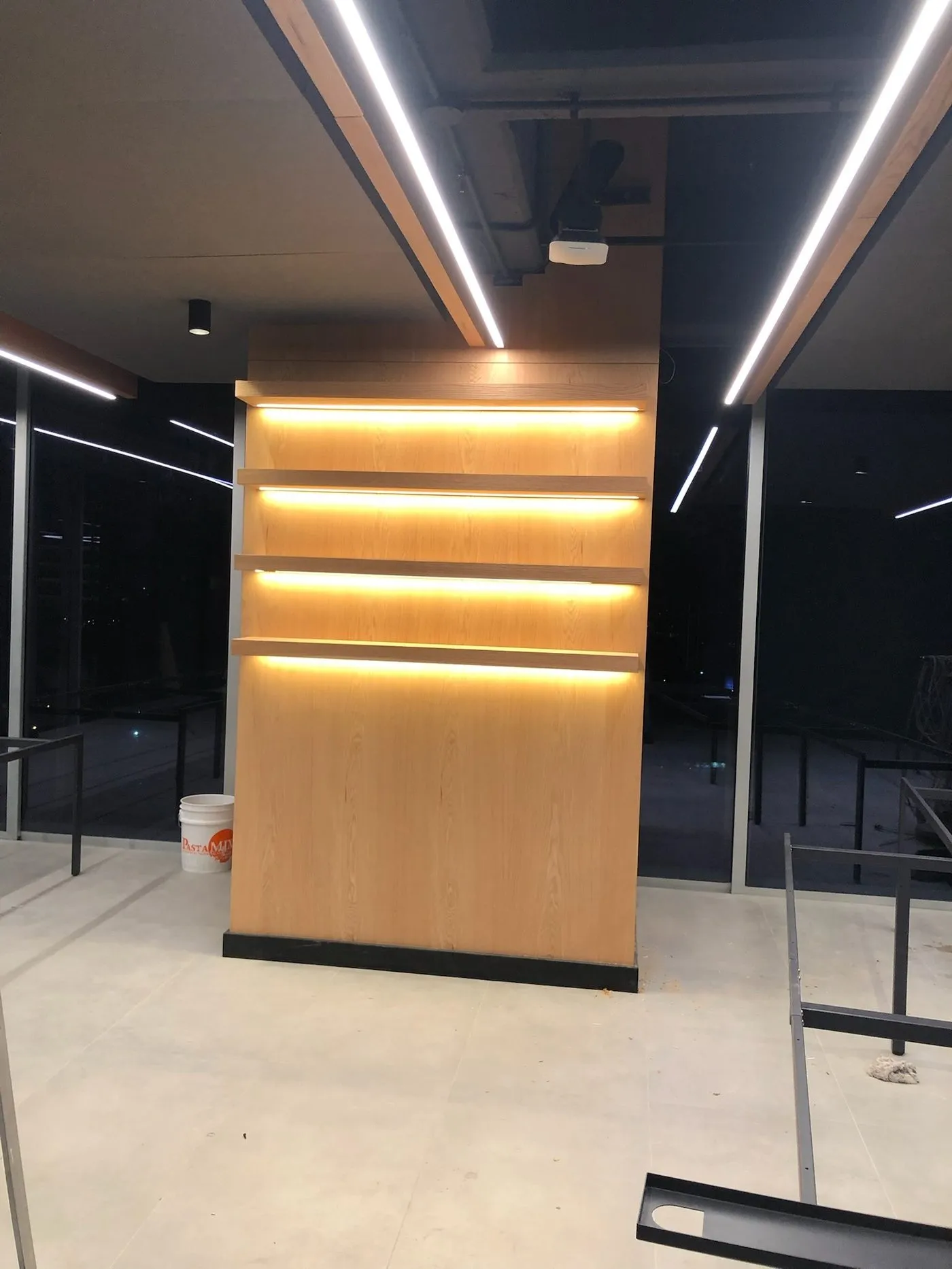 Mueble divisor de madera con repisas iluminadas y luminarias lineales en el techo
