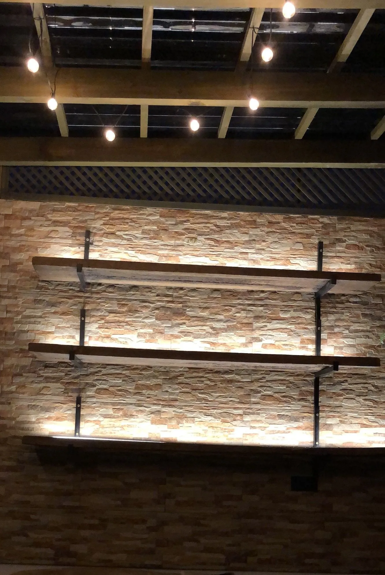 Muro de piedra con repisas de madera iluminadas con LED