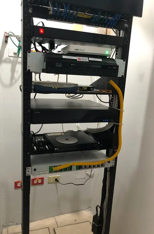 Rack de comunicaciones montado en pared con equipos y cable amarillo